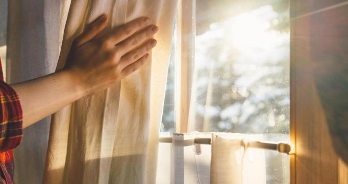 hand opening curtain to let sunlight in