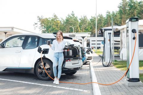 woman with a coffee leaning against a charging car